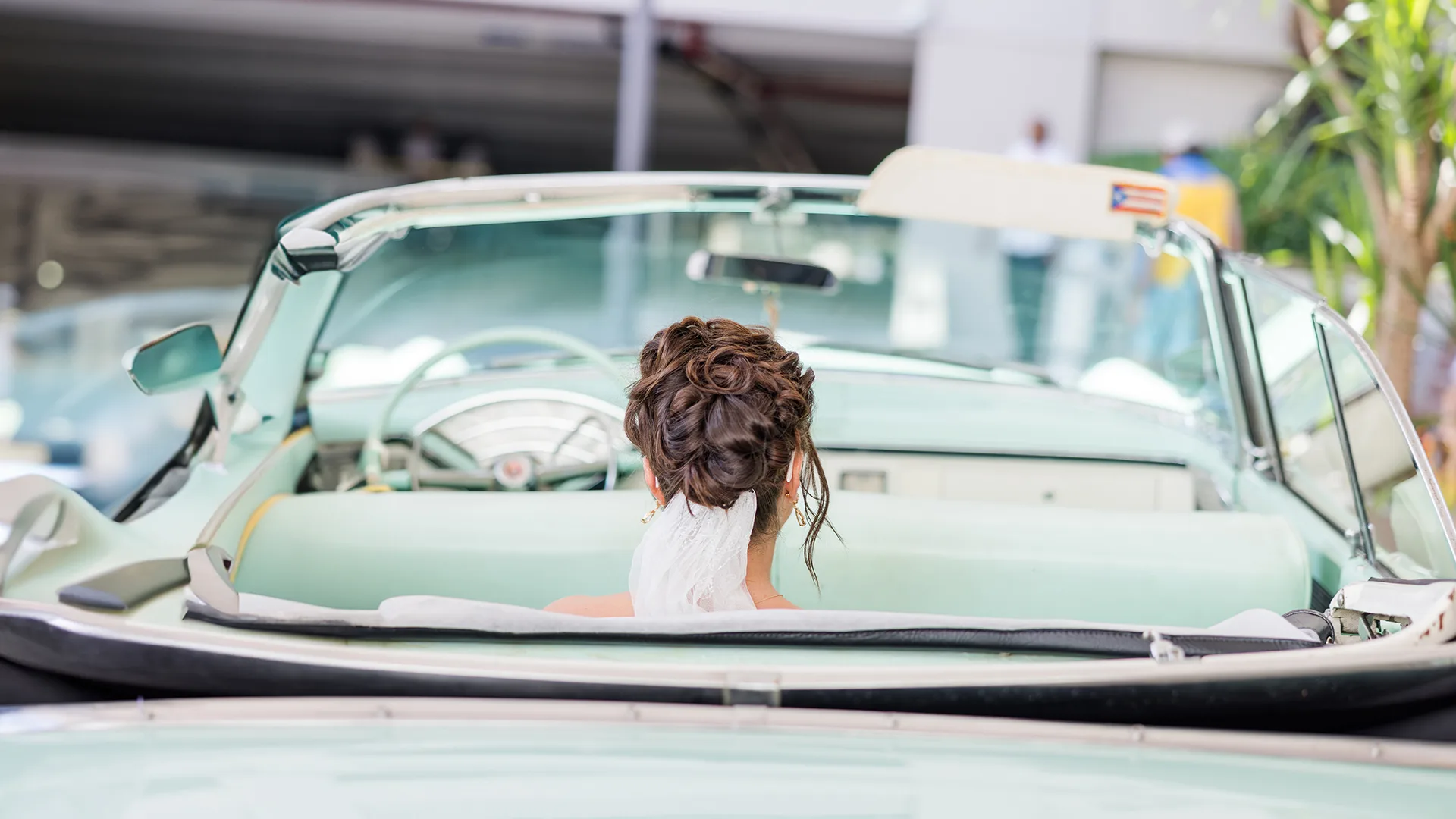 A photo taken from the rear of a classic car with the bride sitting in the rear seat relaxing before her ride to her wedding ceremony.