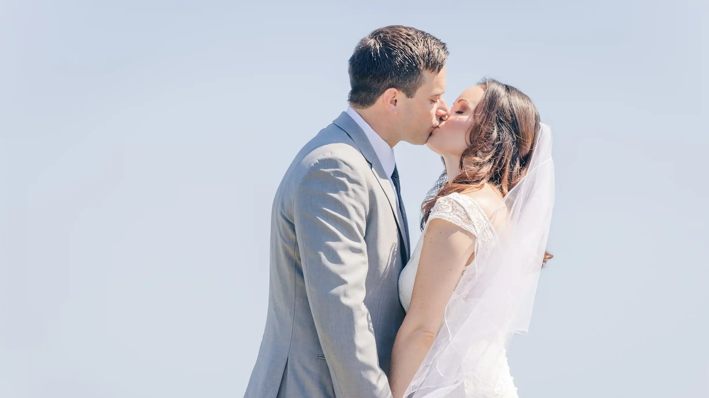 Bride and groom sharing a sweet kiss with a beautiful bright blue sky in the background at the Jersey Shore.