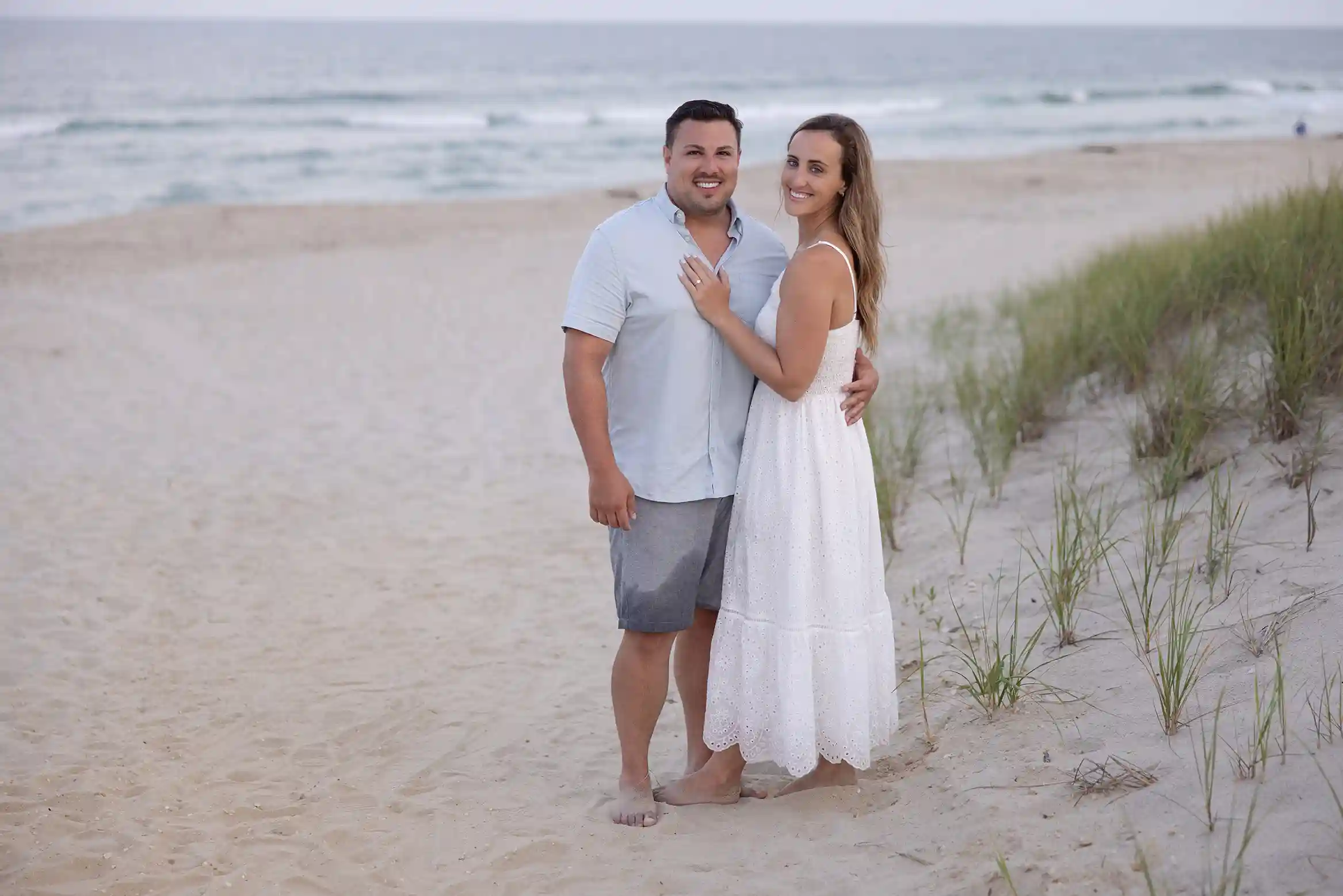 Sunset engagement session at Long Beach Island, NJ. Couple in casual attire standing in the sand next to the ocean.