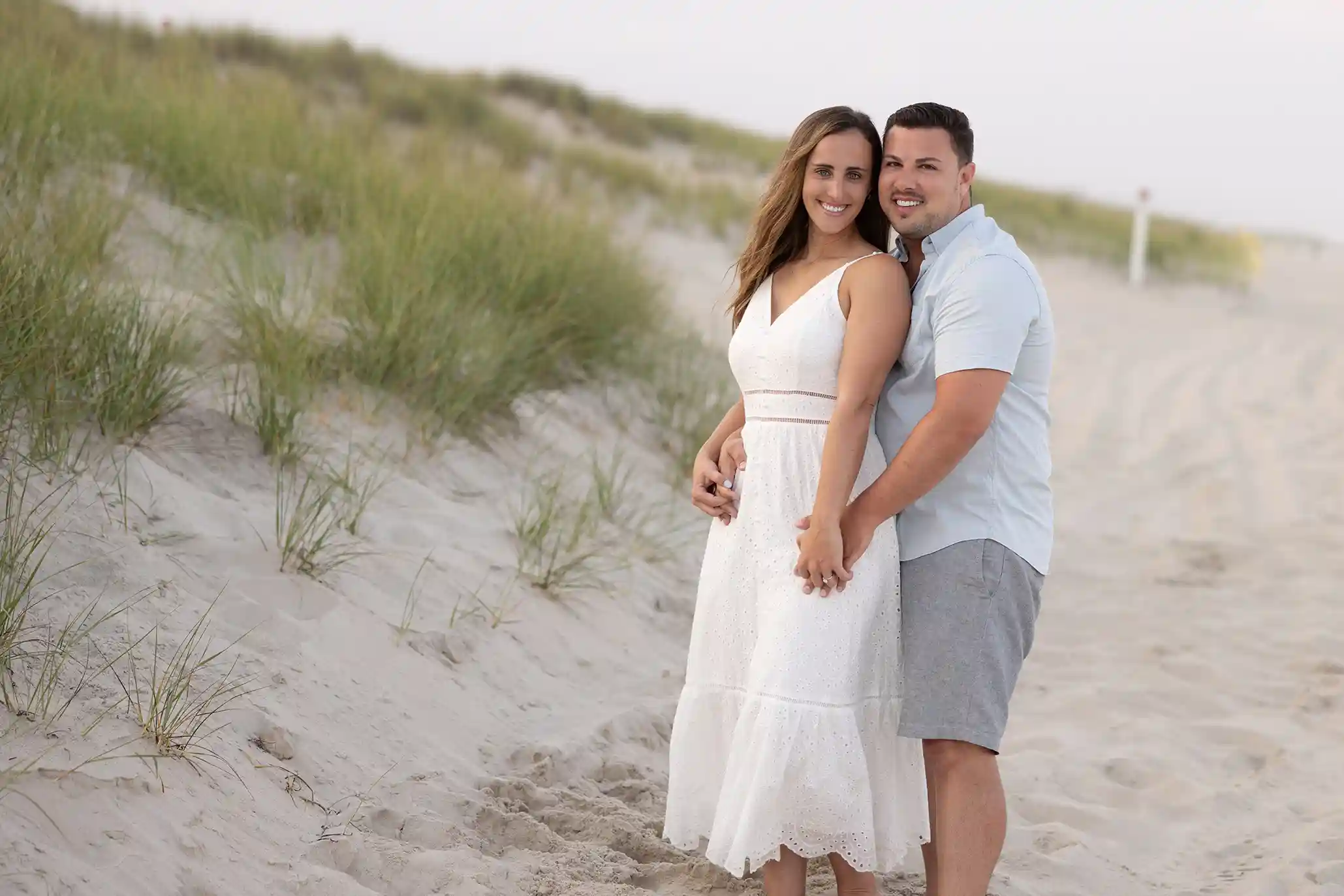 Sunset engagement session at Long Beach Island, NJ. Couple in casual attire standing in the sand next to the ocean.