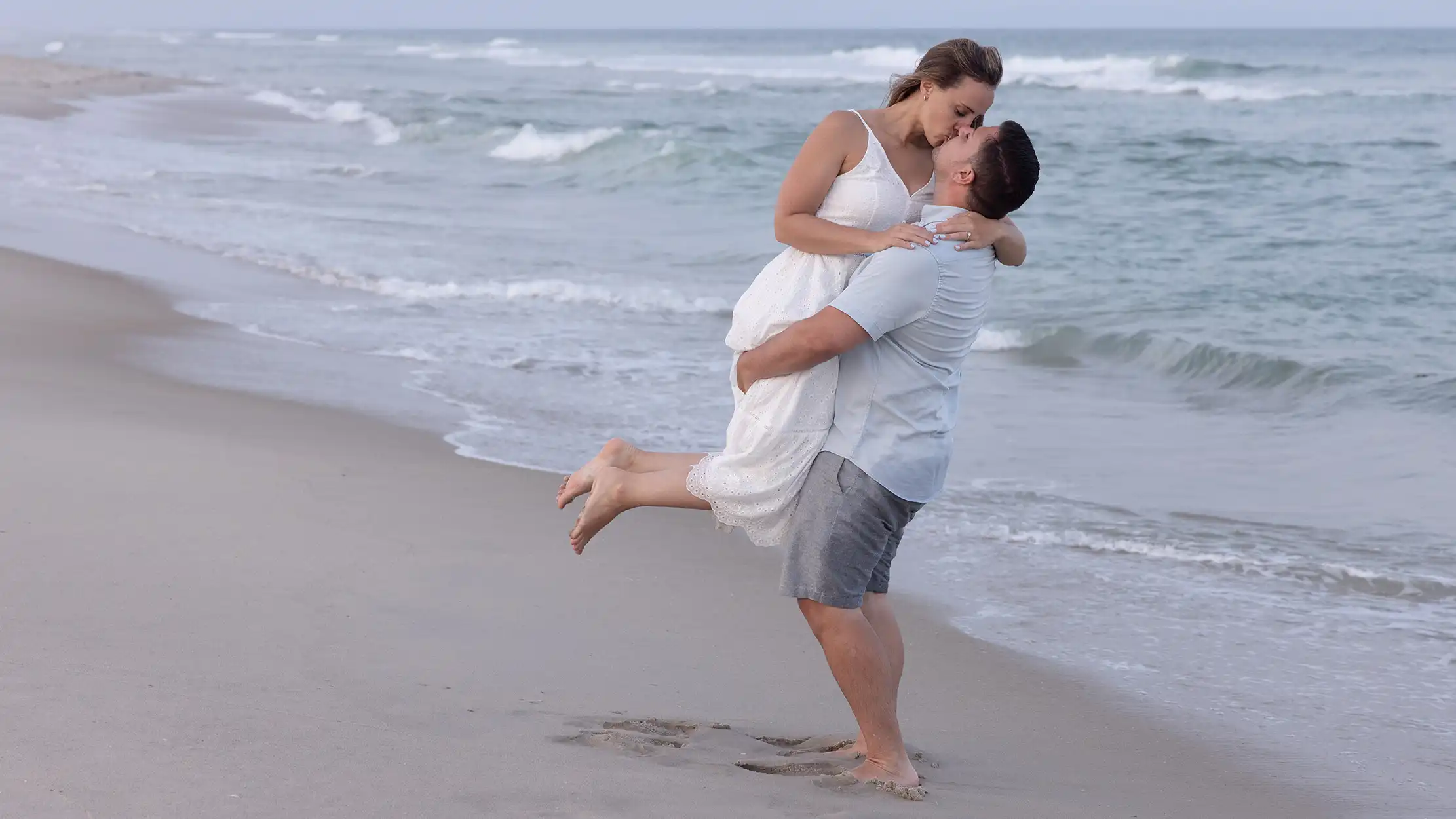 Sunset engagement session at Long Beach Island, NJ. Couple in casual attire standing in the sand next to the ocean.