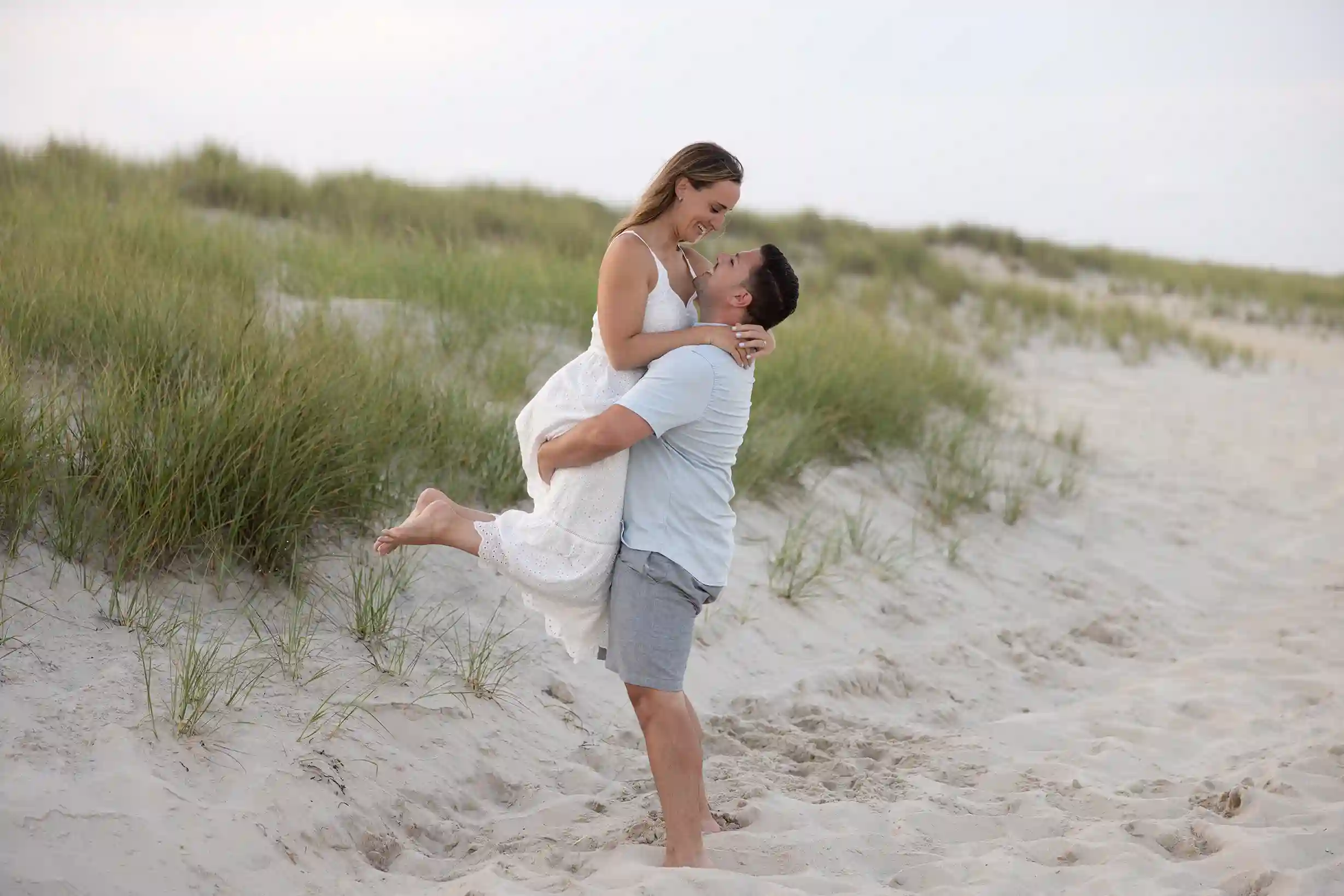 Sunset engagement session at Long Beach Island, NJ. Couple in casual attire standing in the sand next to the ocean.