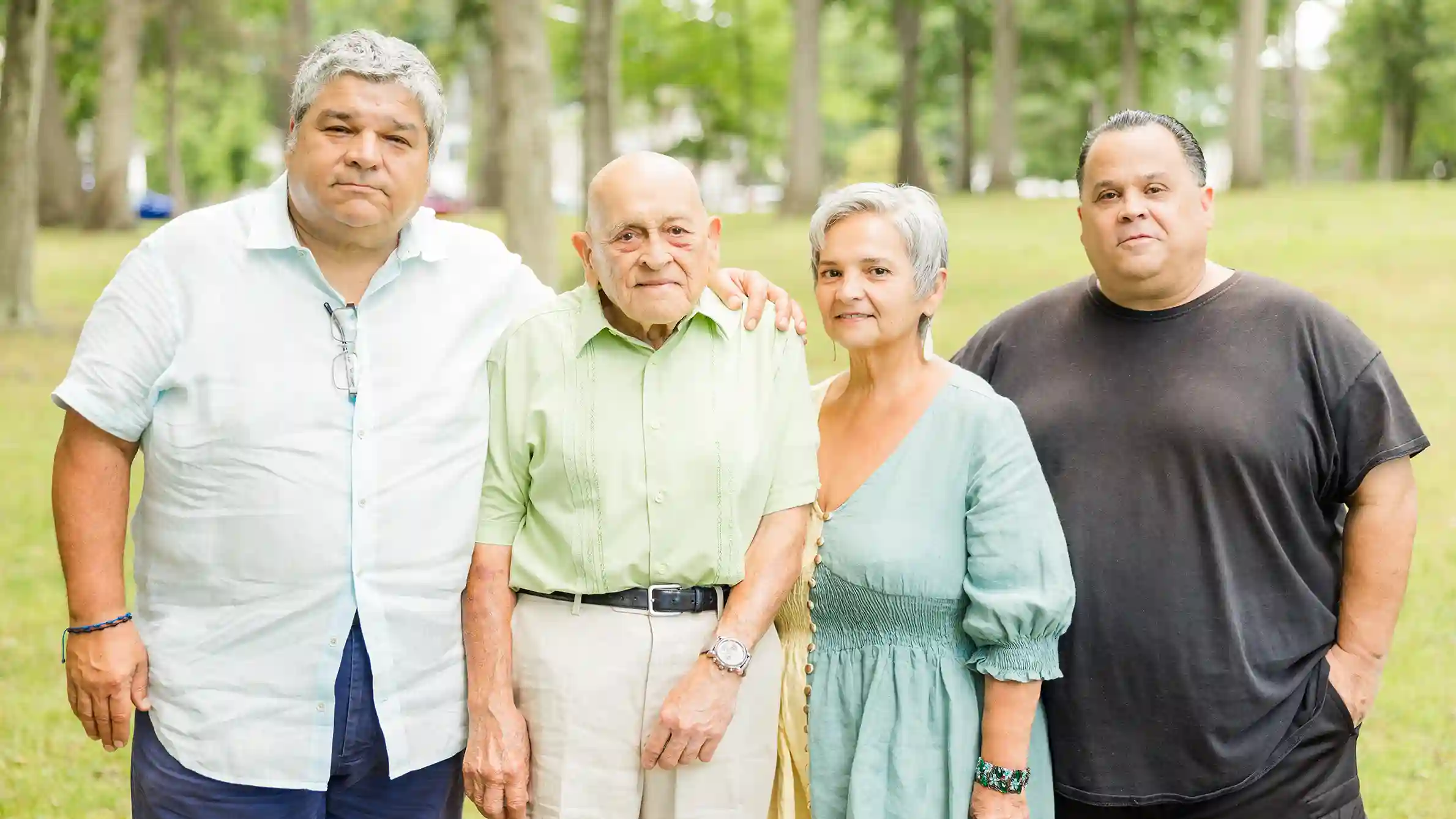 A family posing at a beautiful park on a bright sunny day with husband, wife and children.