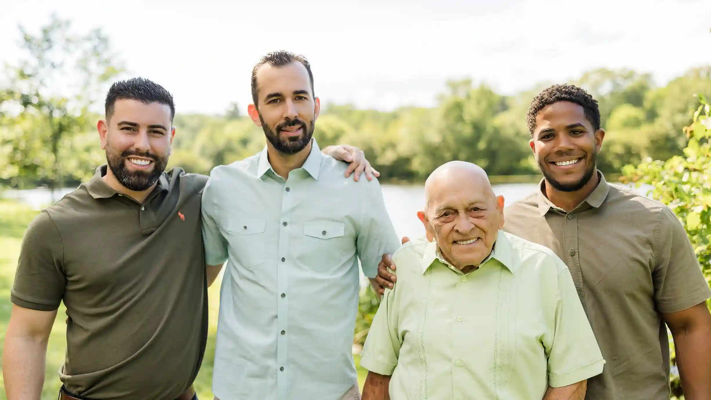 A family photograph of a grandfather with his grandsons at a scenic park with a lake in the background.