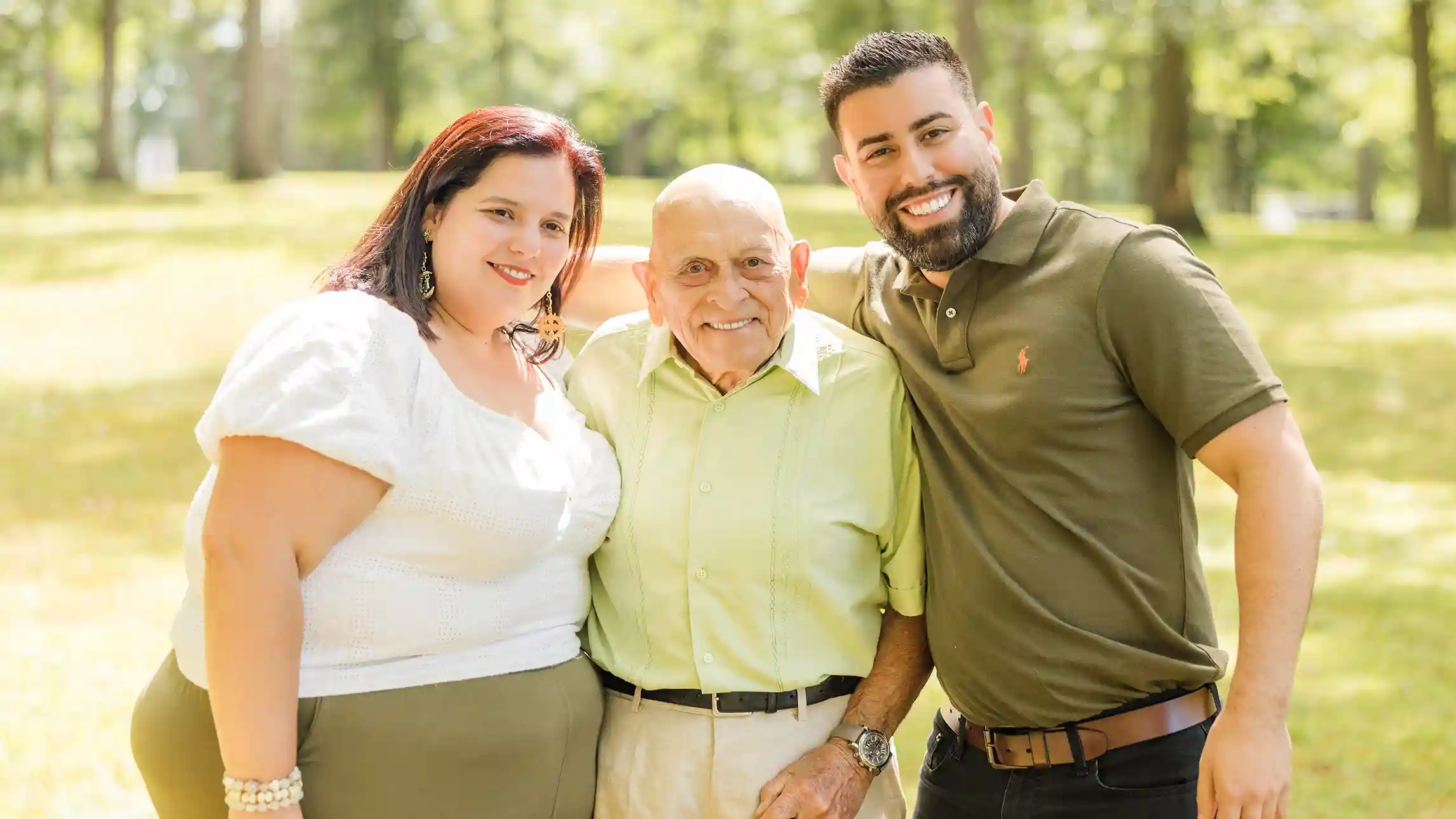 A family photograph during a beautiful sunny day of a grandfather with his niece and nephew at a scenic park with a lake in the background.