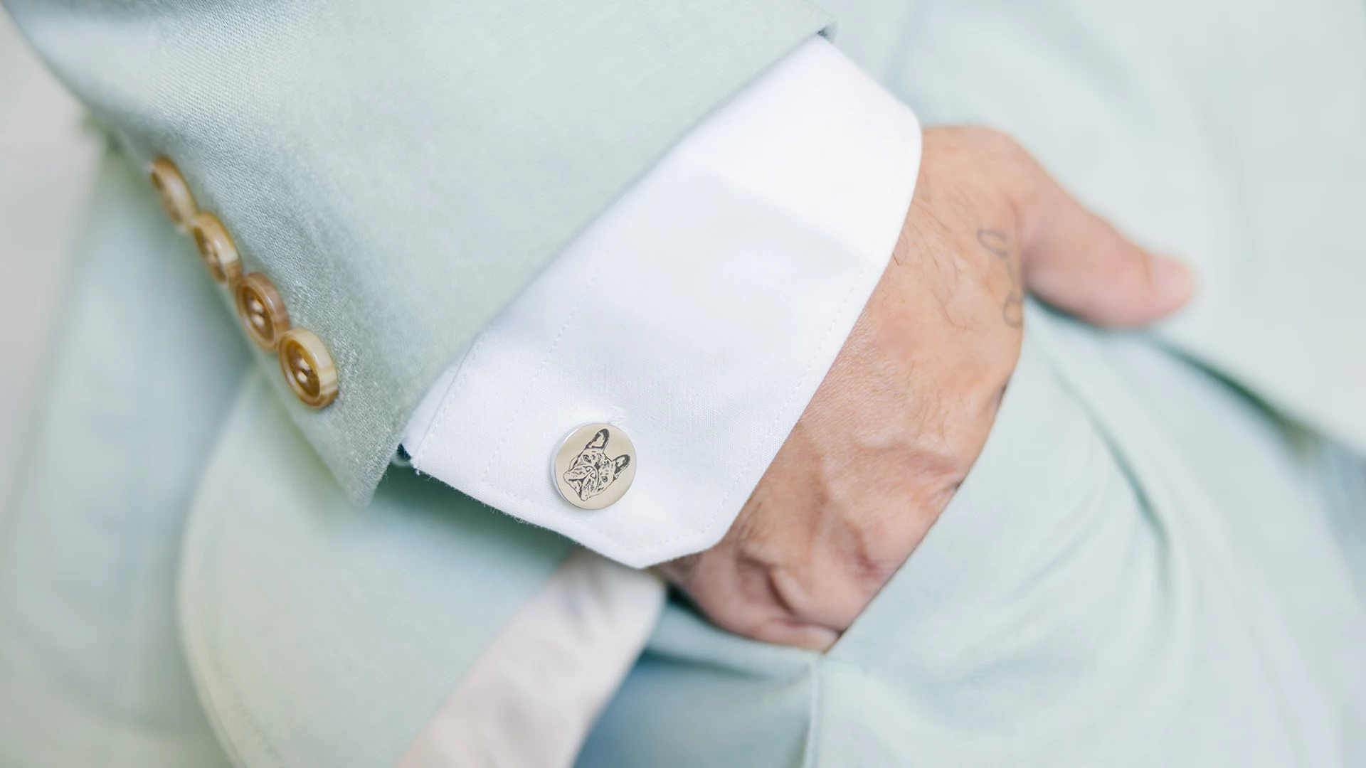 A close-up of the grooms hand in his suite pocket showing the beautiful teal suit with custom engraved cufflinks of this dog, Summer.