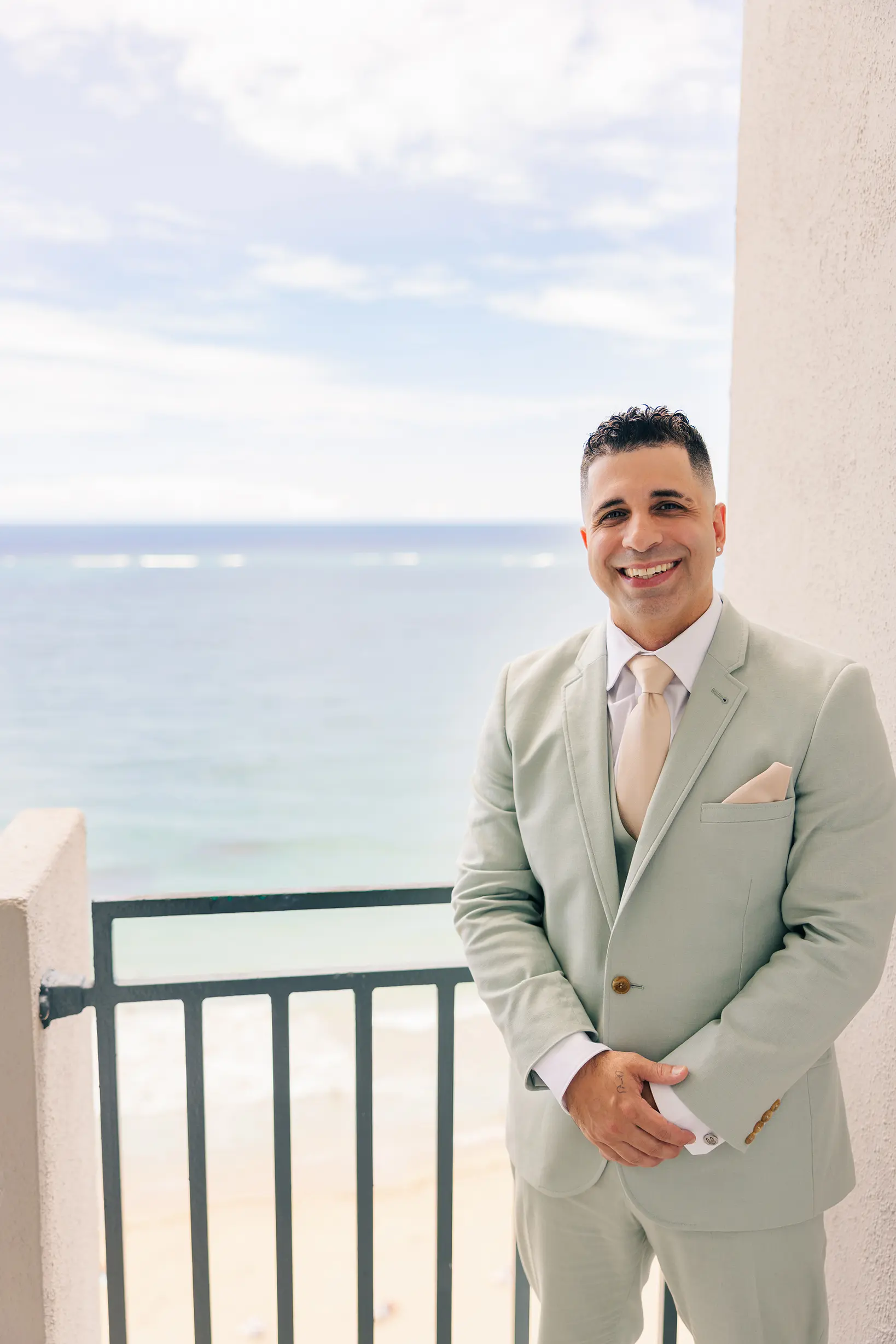 A groom standing outside in Puerto Rico dressed in a suite with an ocean-view background exited for his wedding.