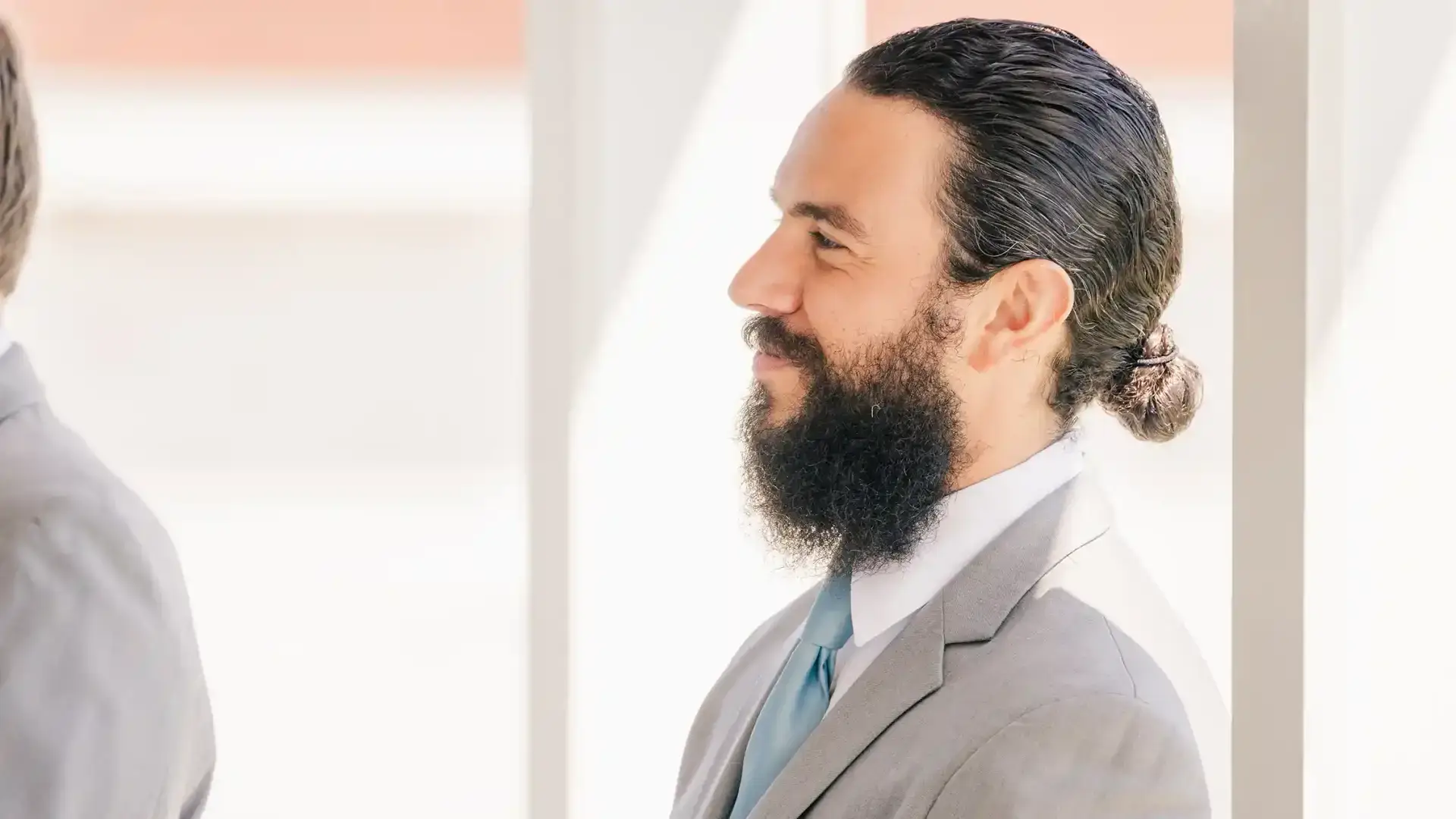 Groomsman smiles warmly at bride and groom during sunny Barnegat Light, NJ wedding ceremony.