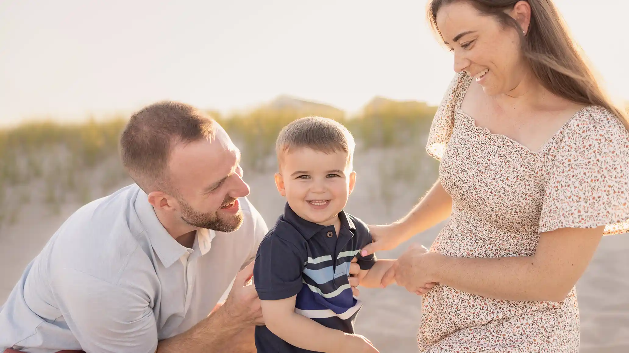 A smiling little boy with his parents, posing for a photo on a sunny New Jersey beach.