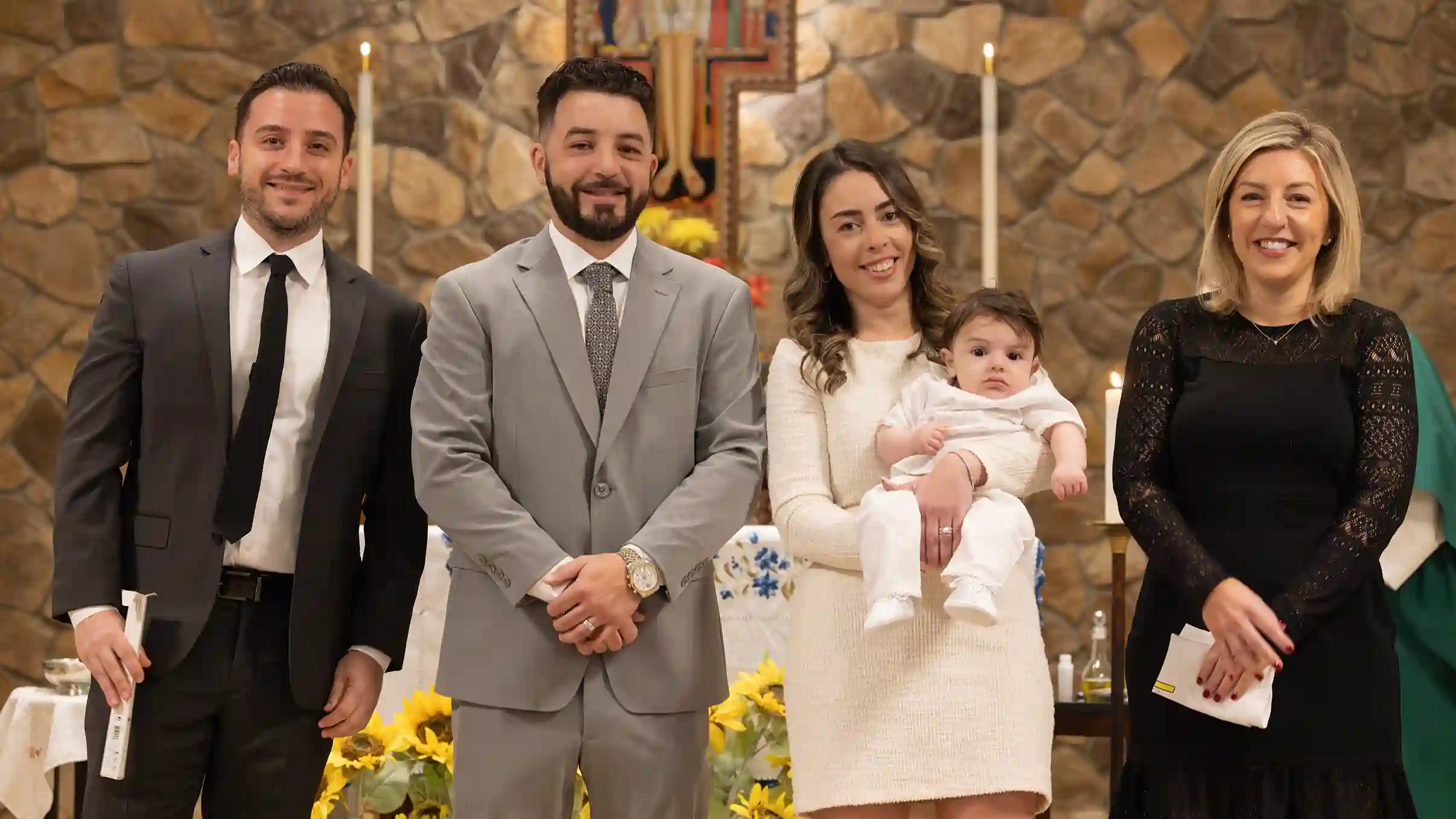 A baby boy being held by his mother at the alter with the godfather and god mother after being baptized.