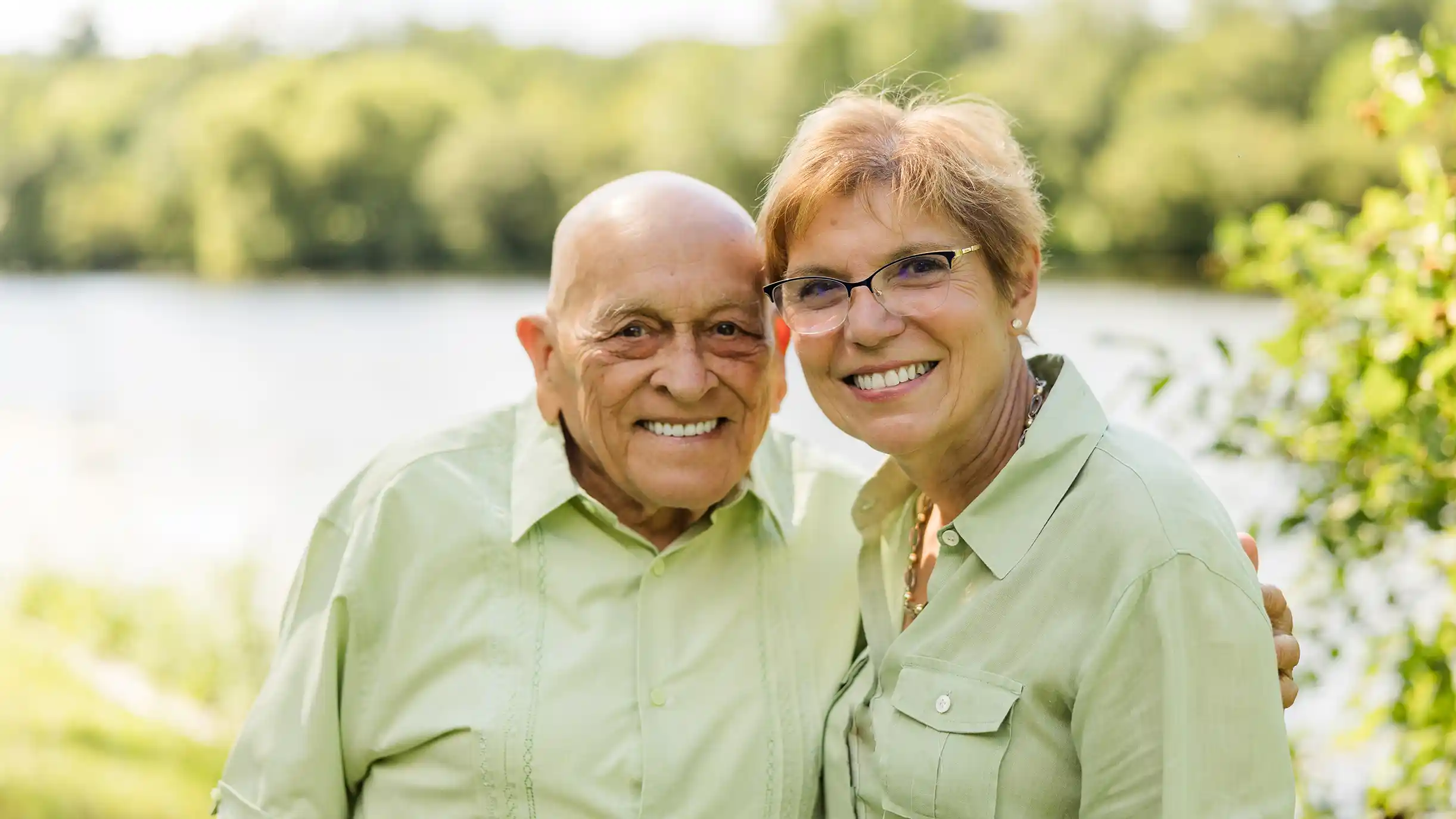 A family photograph of a grandfather with his wife at a scenic park with a lake in the background.