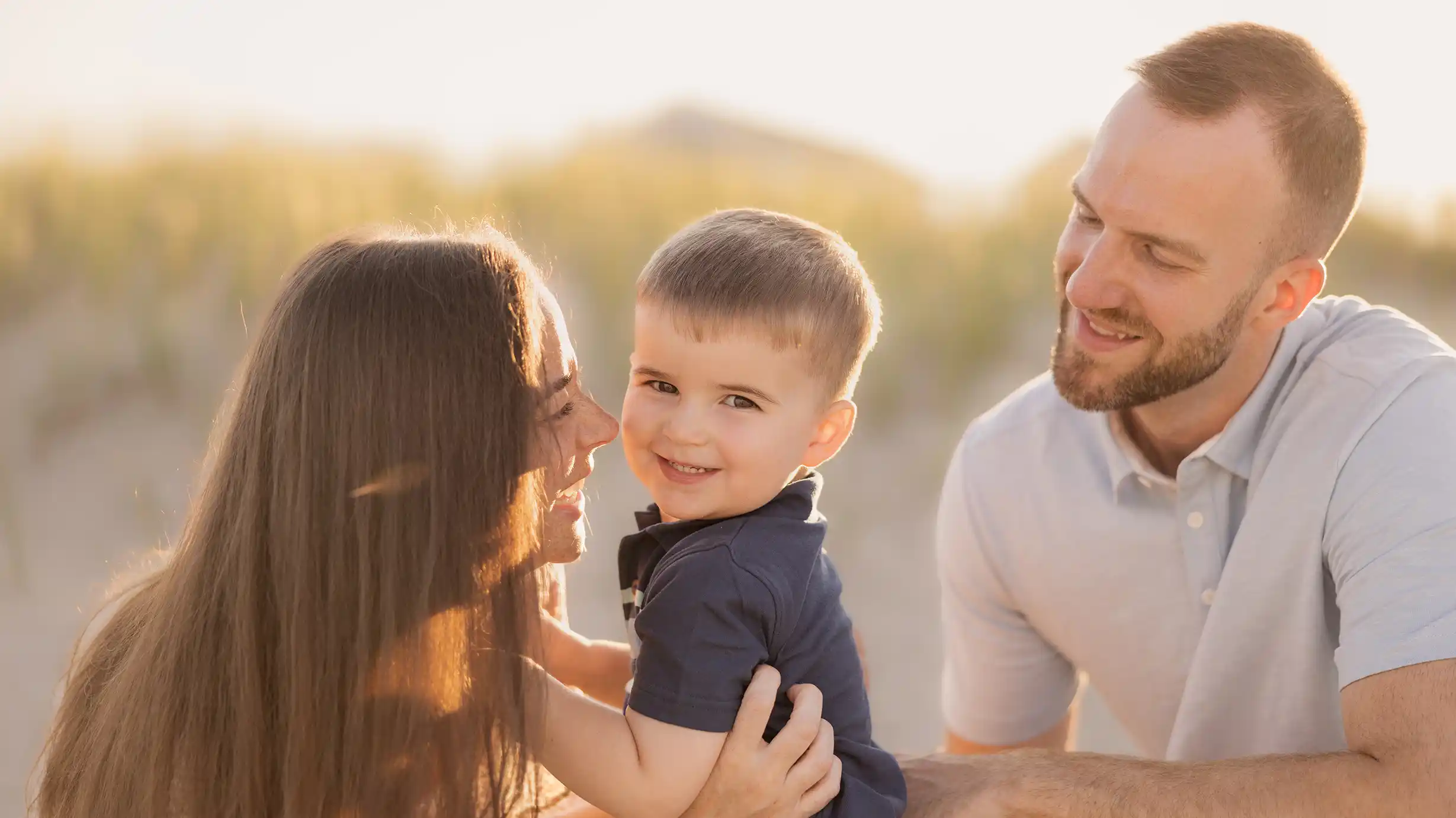 A smiling little boy with his parents, smiling at the camera at a sunny New Jersey beach.