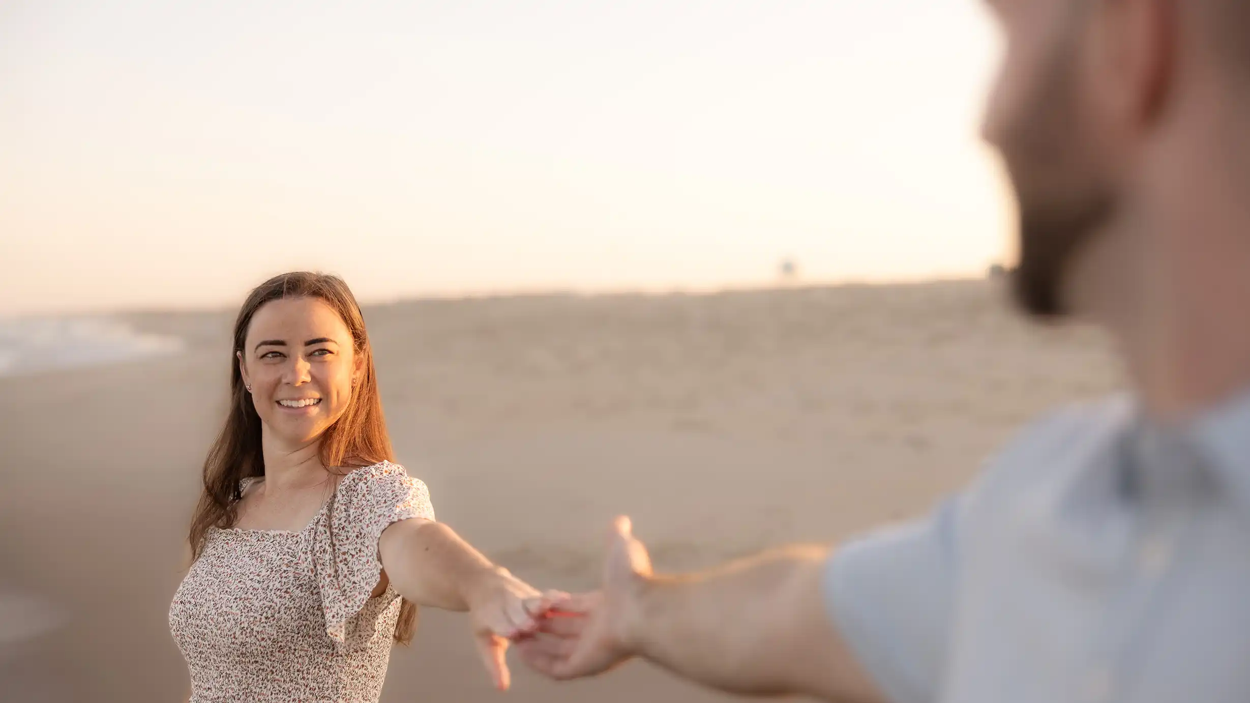 Excited parents-to-be holding hands at the beach. Photo is taken from the husbands perspective.