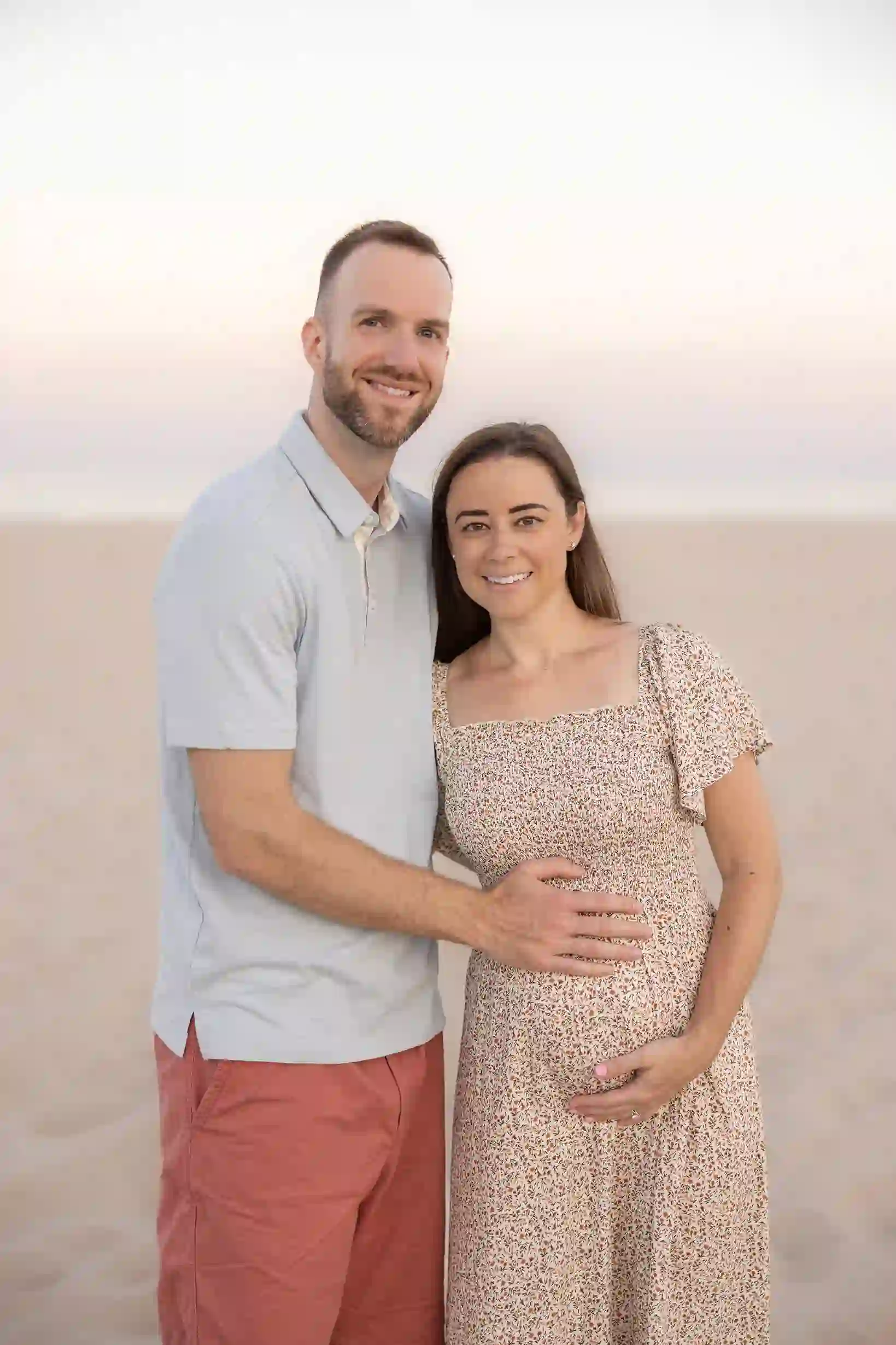 Excited parents-to-be, husband filled with joy as he touches his pregnant wife's belly with the beautiful beach behind them.