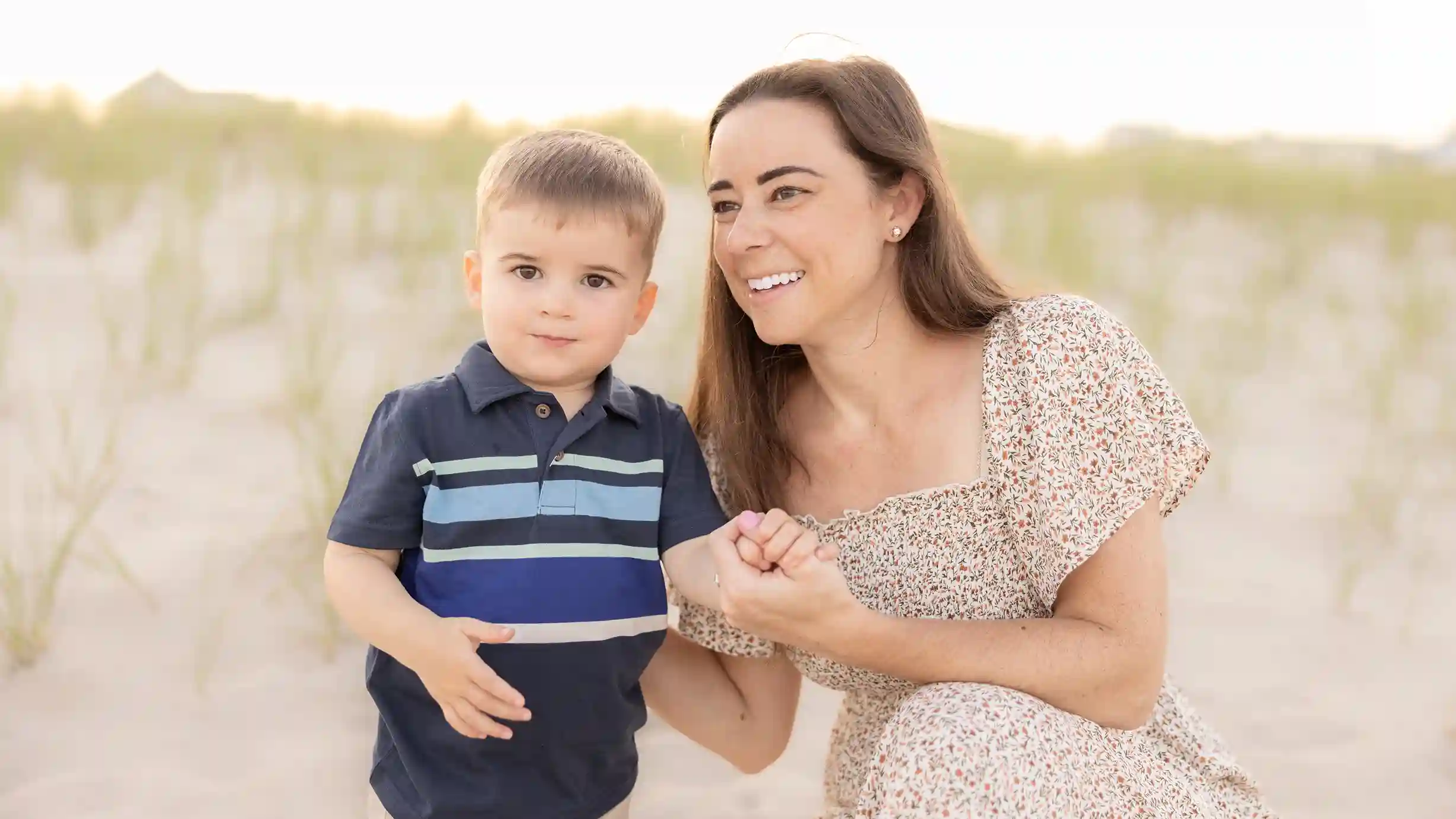 A little boy looking at the camera with his mother during their photoshoot at the beach.