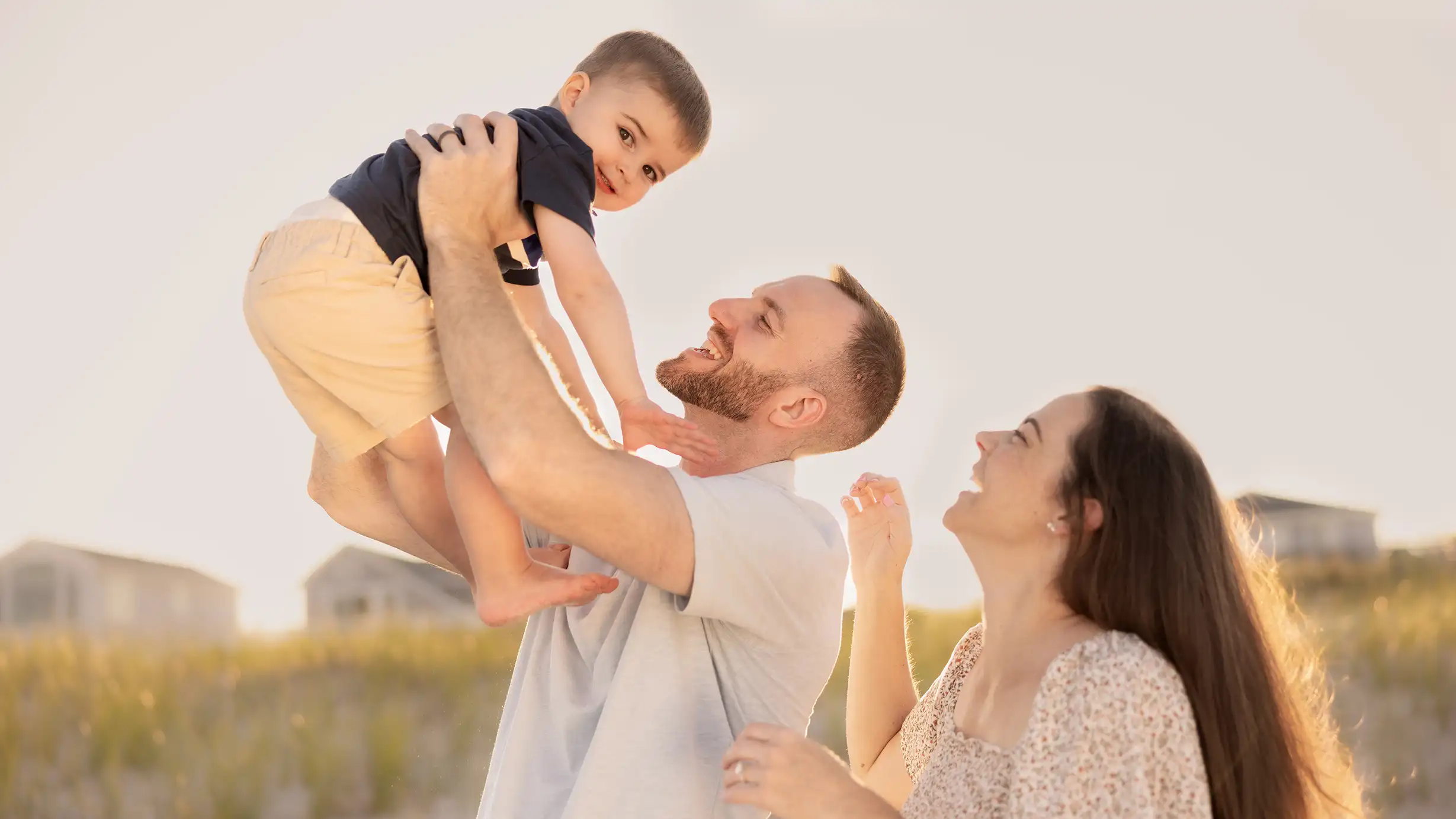 A smiling little boy with his parents, posing for a photo on a sunny New Jersey beach.