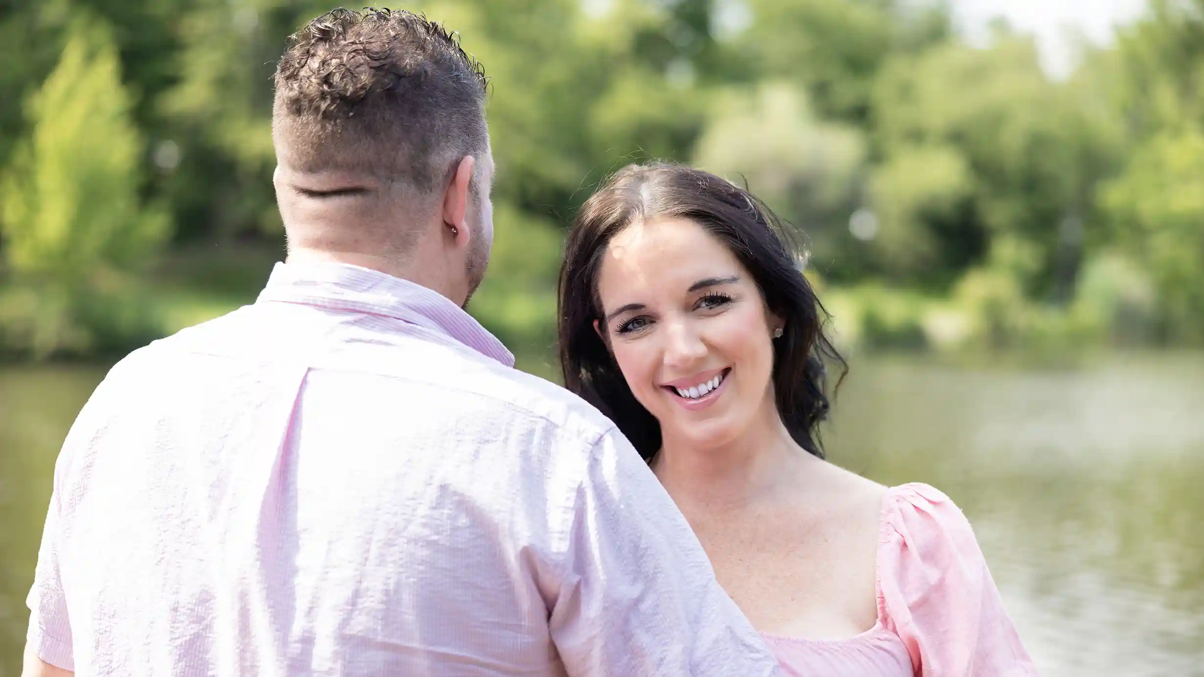 Wife radiates joy while embraced by her husband on a beautiful sunny day.