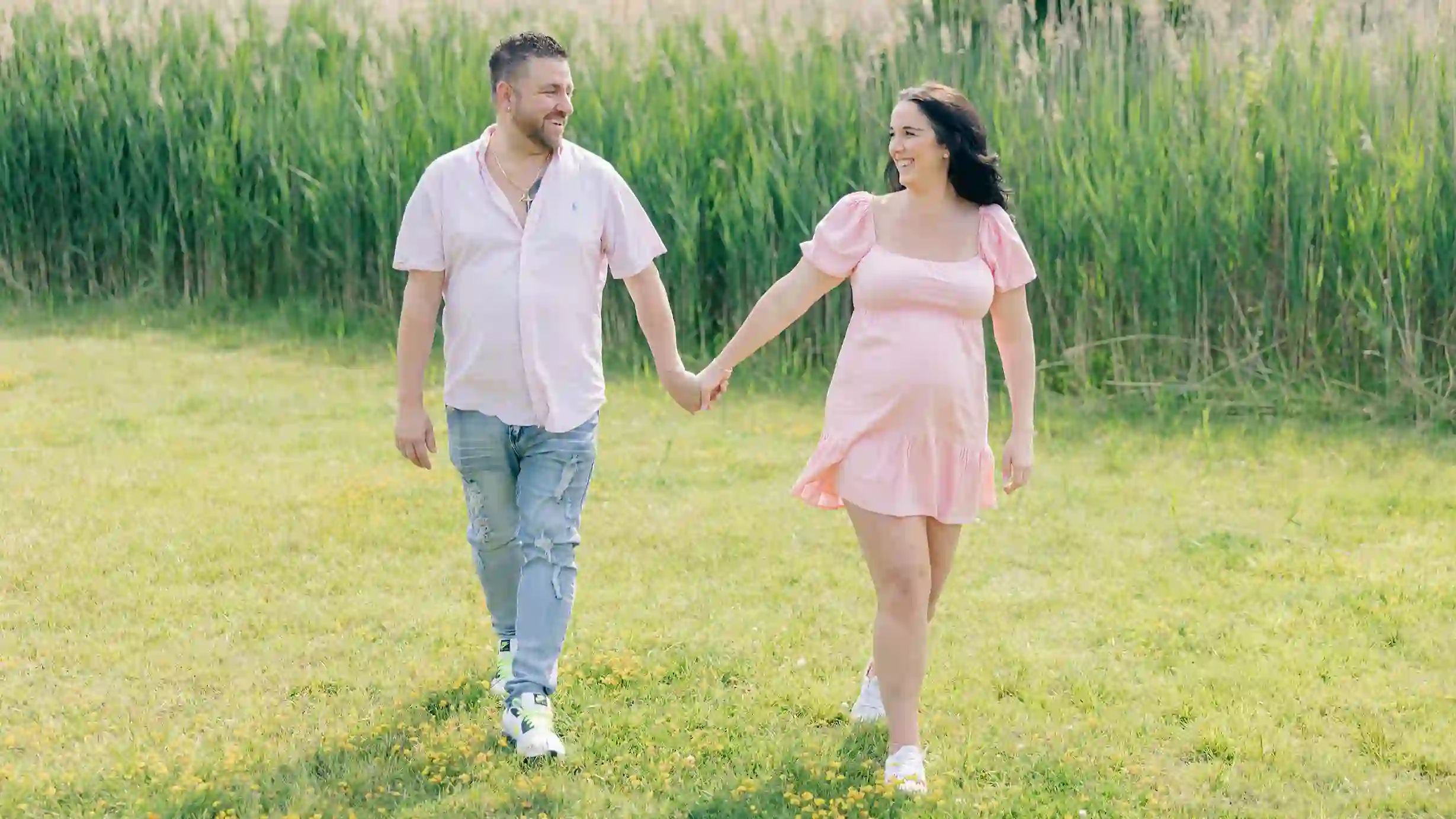 A loving couple, hand-in-hand, enjoys a carefree walk on a sunny day, surrounded by endless green fields.