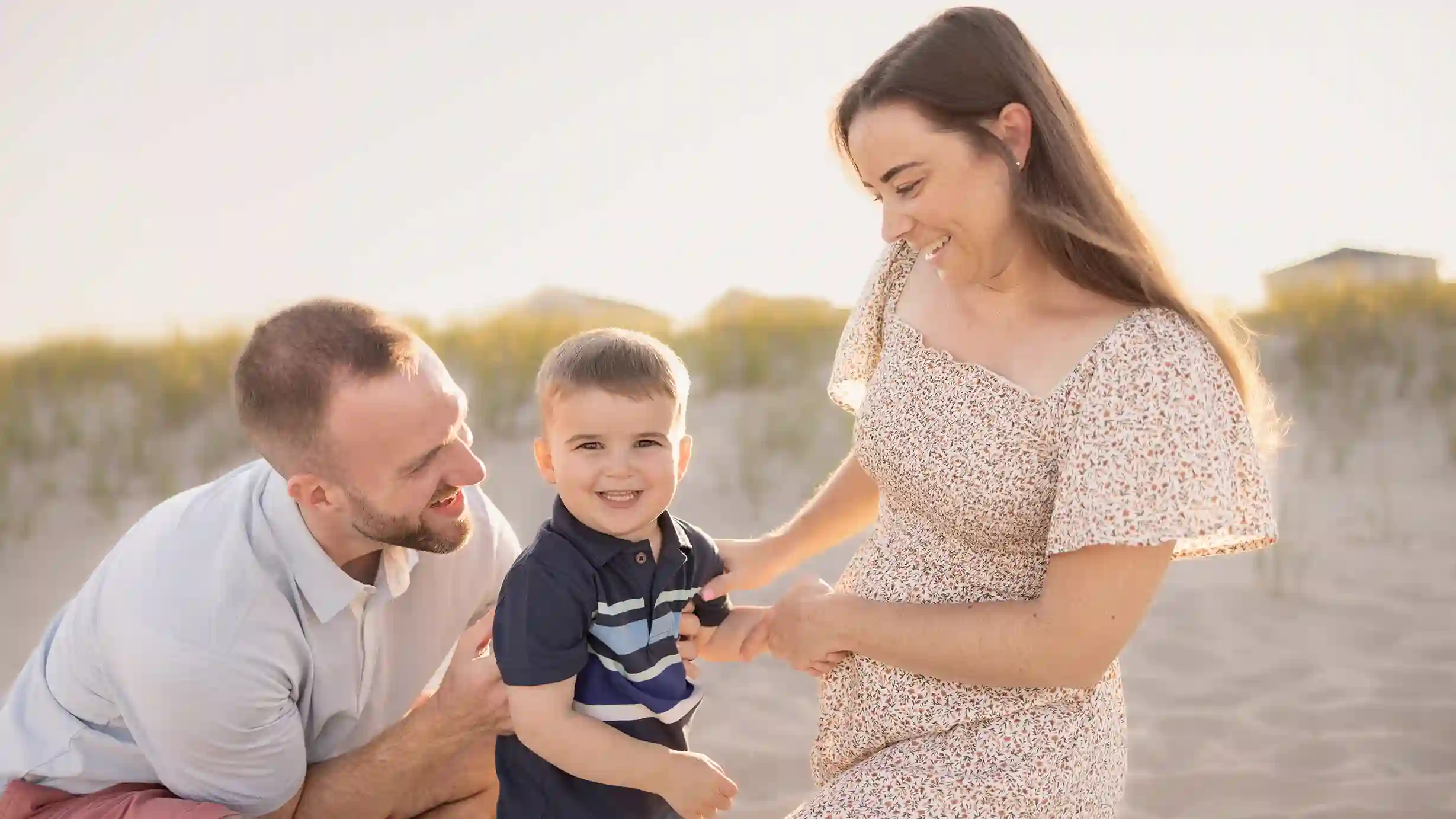 A smiling little boy with his parents, posing for a photo on a sunny New Jersey beach.