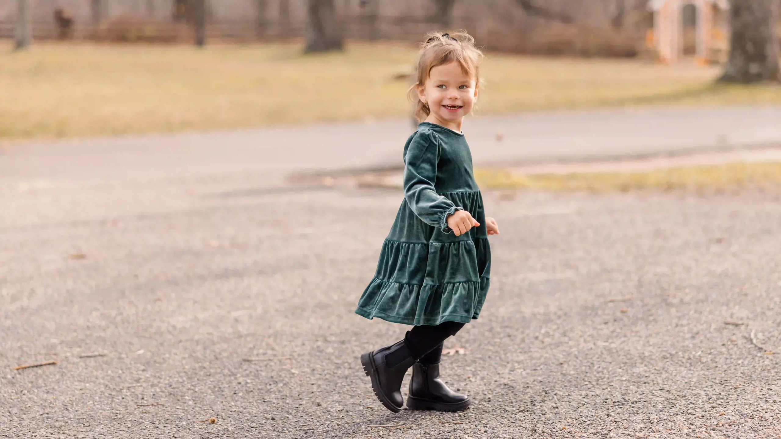 A young girl running in a park playing chase me during her Christmas photoshoot wearing a beautiful green dress.