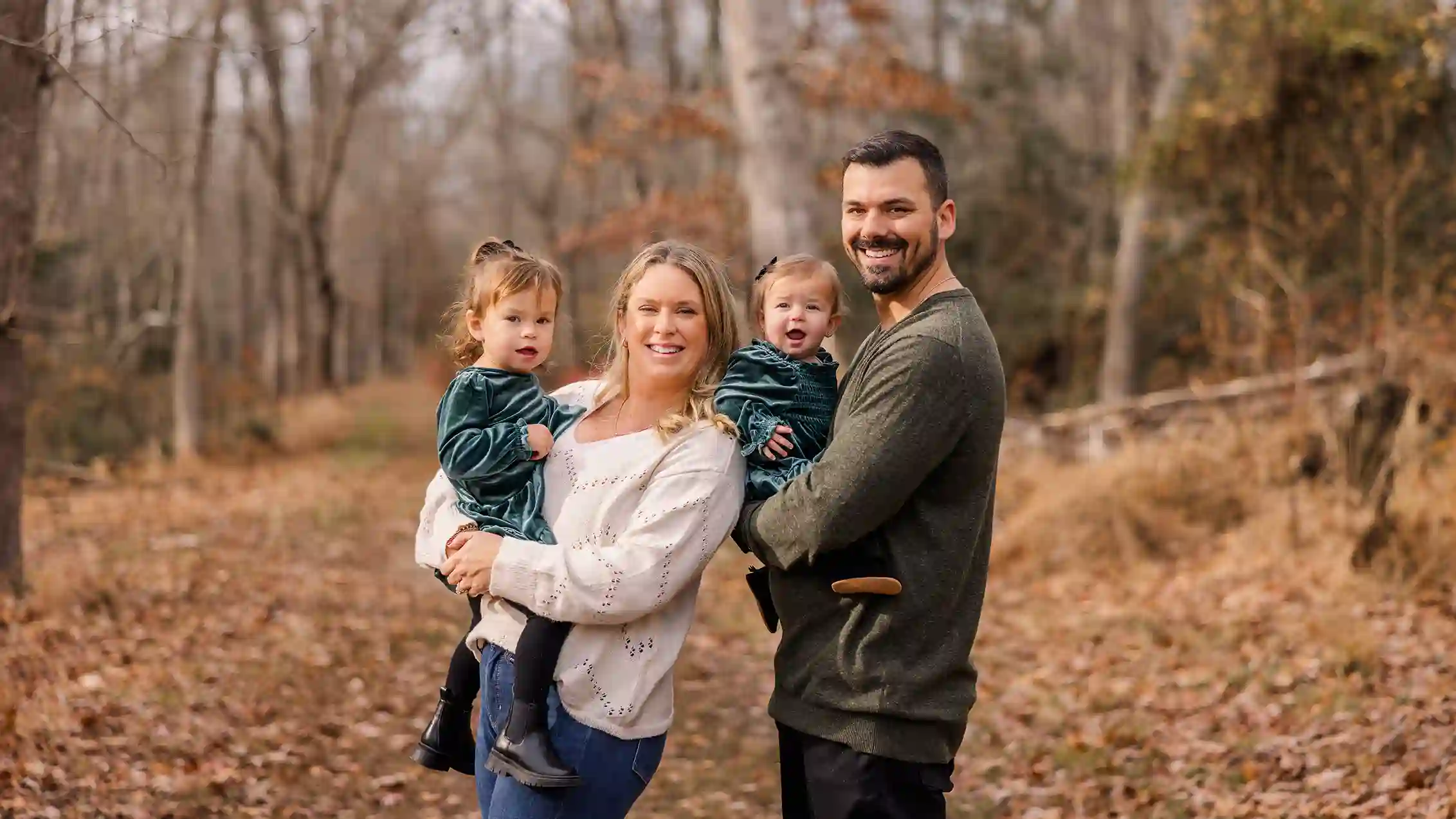 A family taking smiling in the woods for their Christmas photoshoot with a visually captivating fall foliage background.