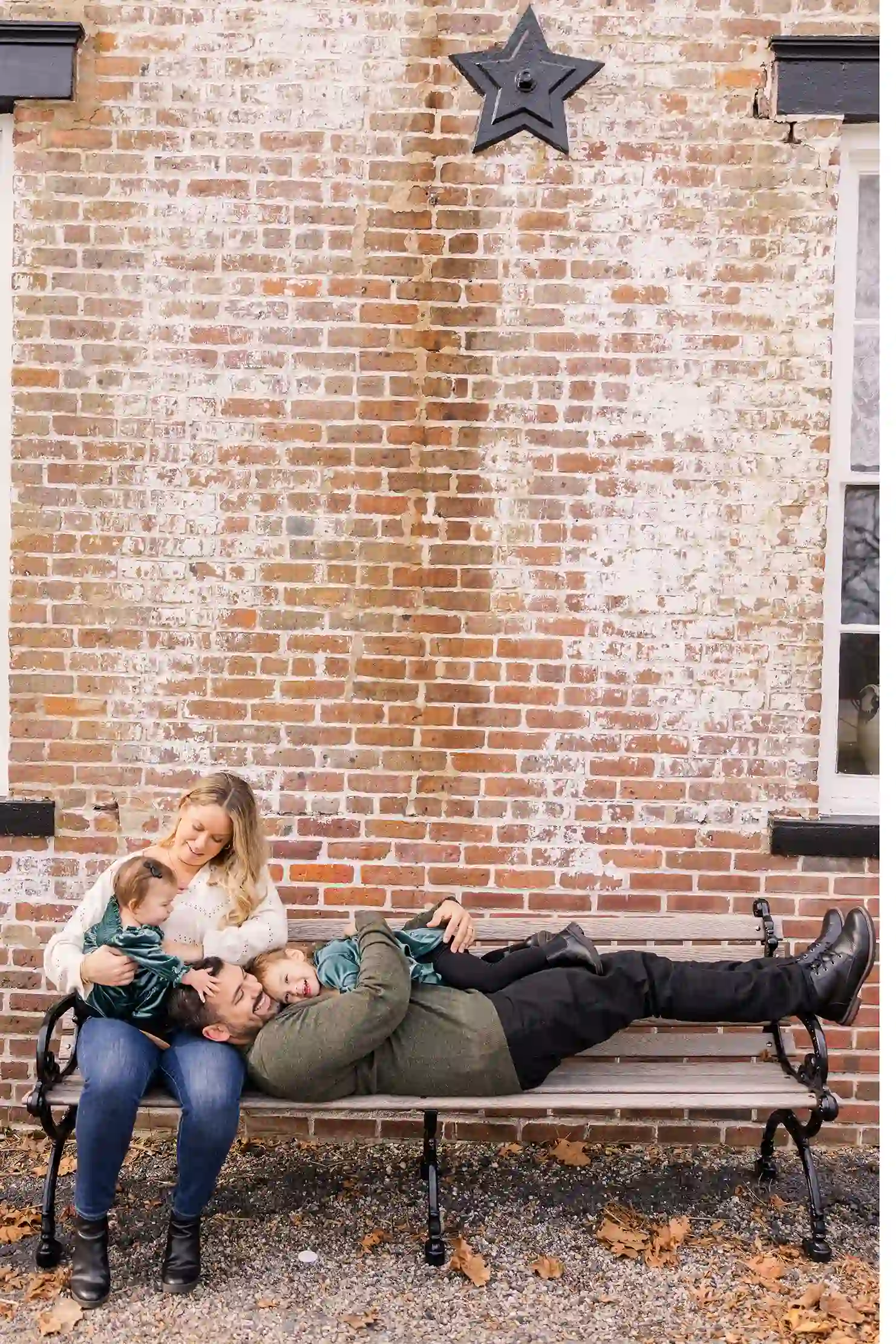 A family on a bench reminiscing of their engagement shoot, now with two beautiful little girls smiling at each other.