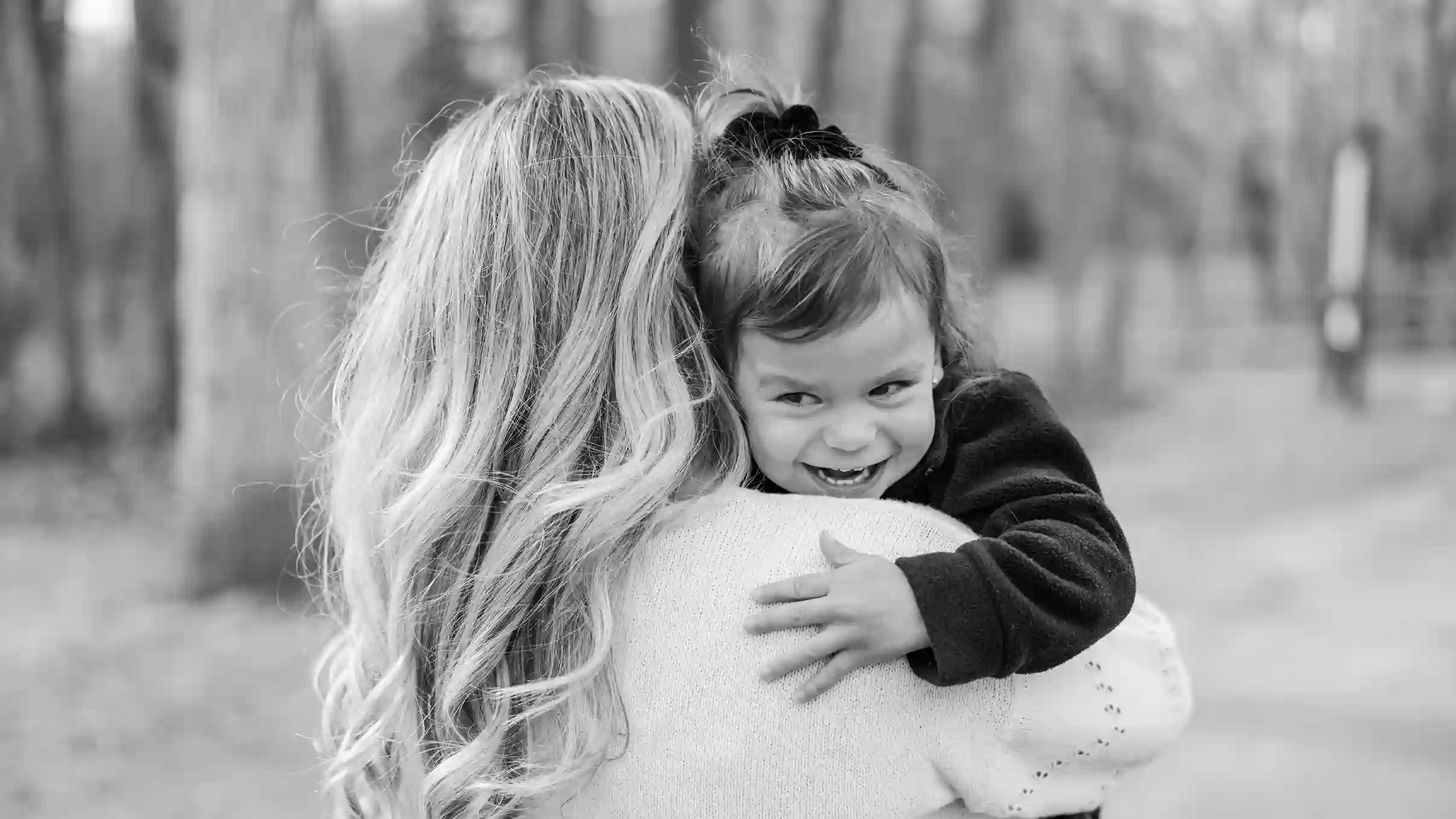 A little girl being carried by her mom walking through the park while happy and snuggling with each other.