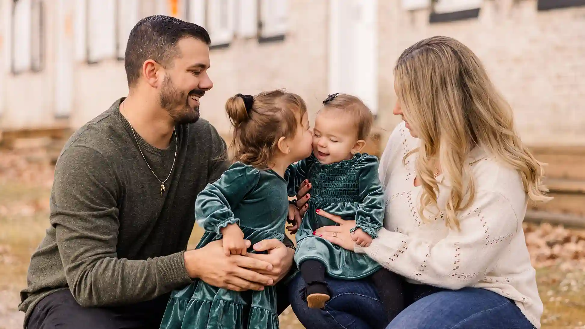 The big sister giving the little sister a kiss during their first Christmas photoshoot together with the parents holding each of them.