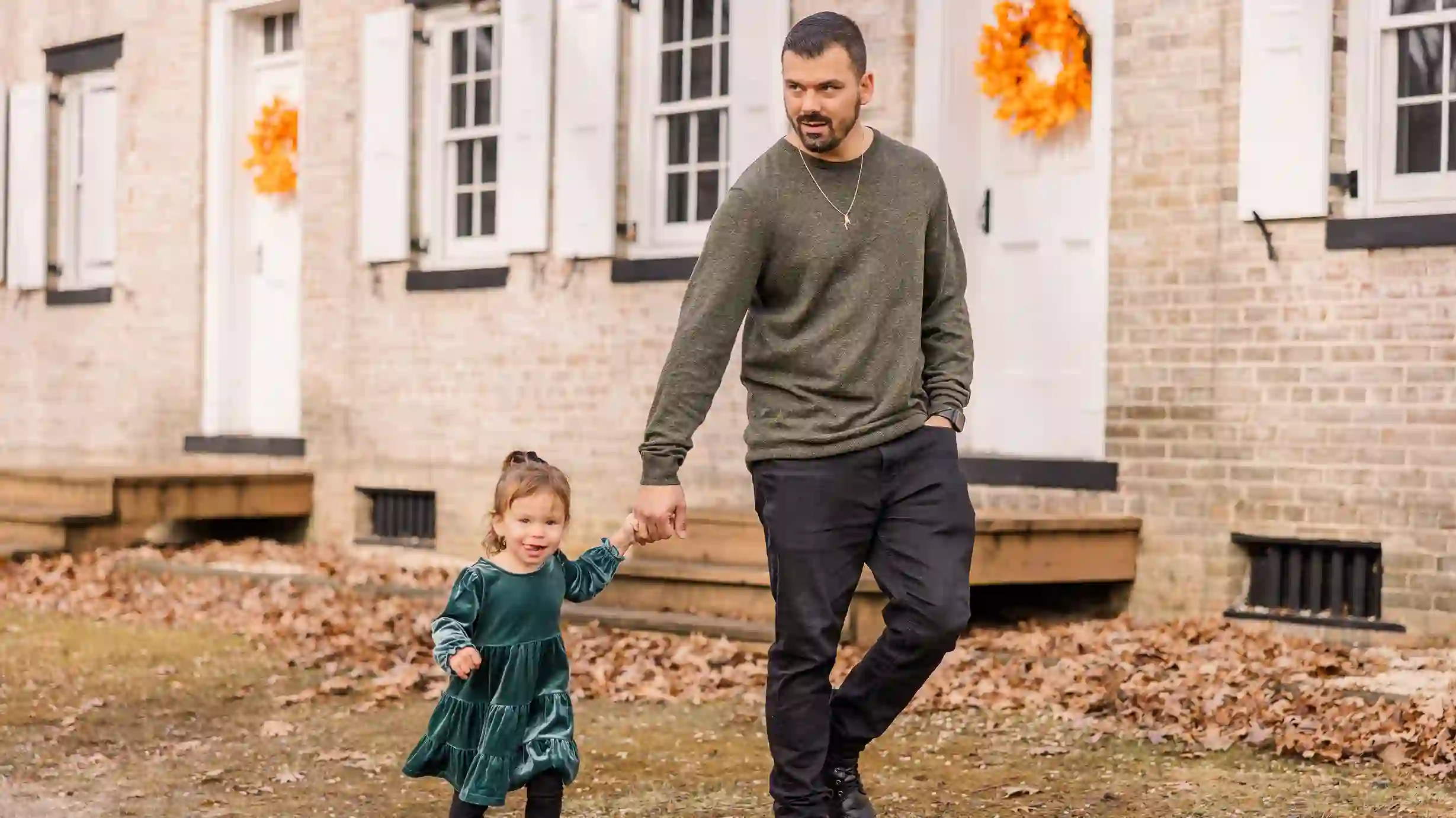 A dad walking in the park with beautiful fall foliage holding his daughters hand.