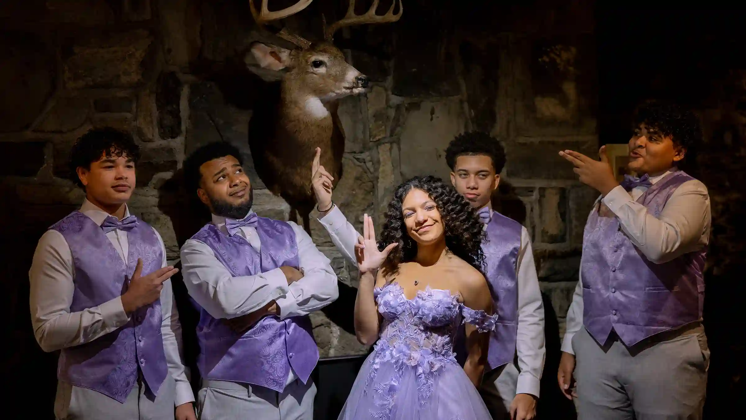 Teenage girl celebrating her sweet 16 her court in a dark and mysterious room with a deer head mounted on the wall.