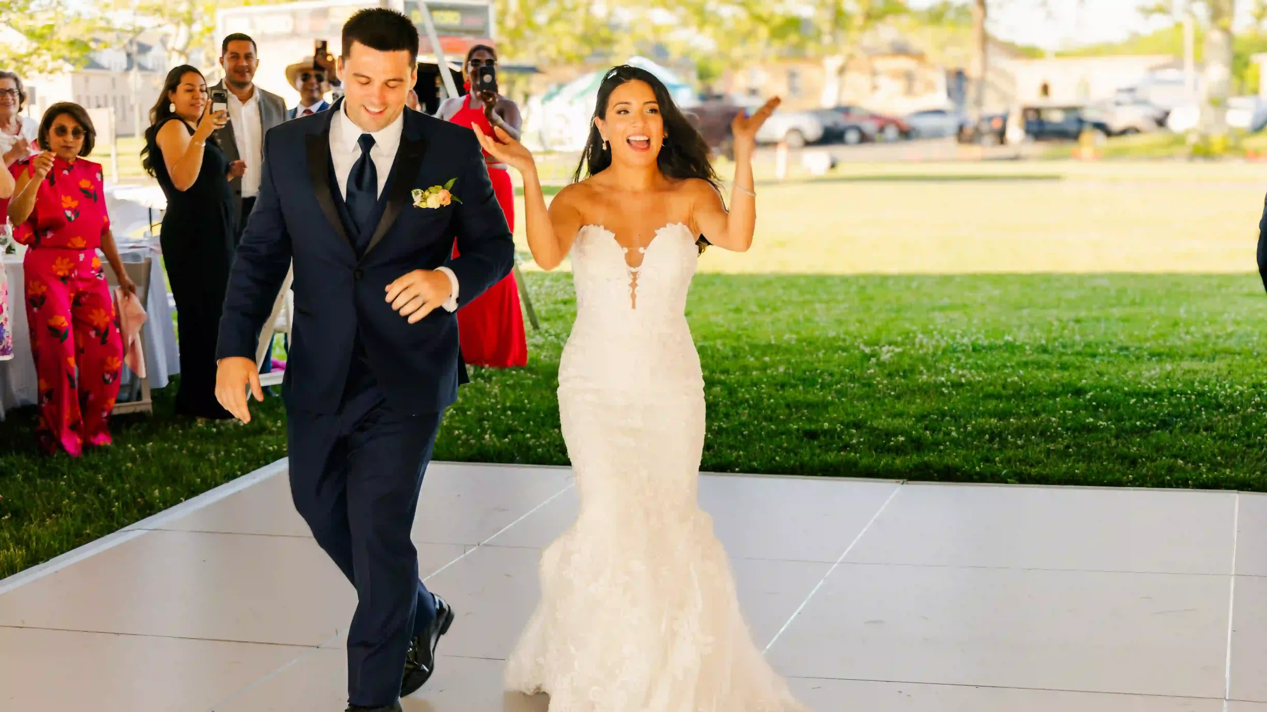 Ecstatic bride and groom clapping during their joyful entrance into their wedding reception, surrounded by happy guests.