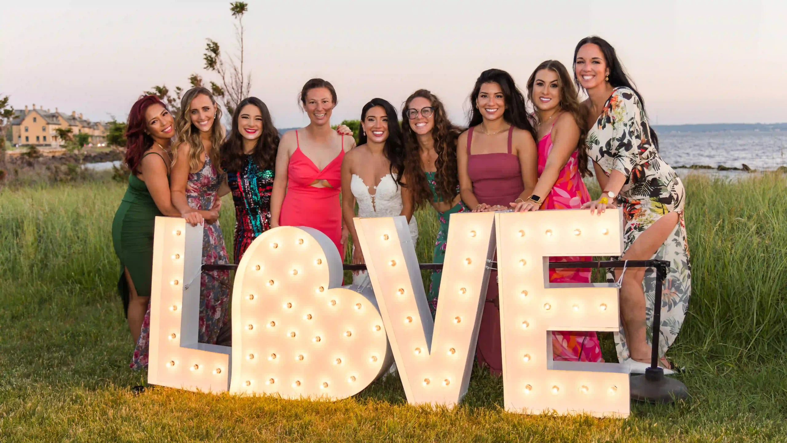 Friends of the bride and groom gather for a group photo, smiling together in front of a large, decorative sign that spells "LOVE".