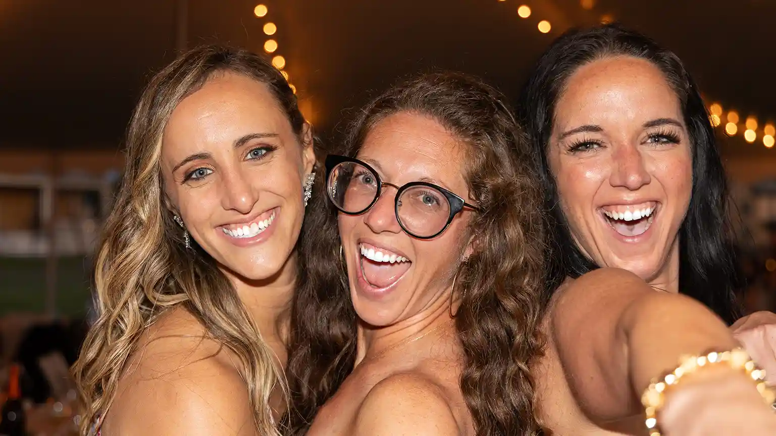 Three friends of the bride and groom point at the camera with vibrant smiling during the dance party at the reception.