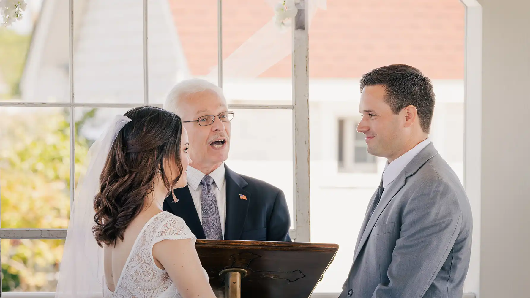 A radiant bride and groom, filled with love, share a smile at the altar while listening to the officiant.